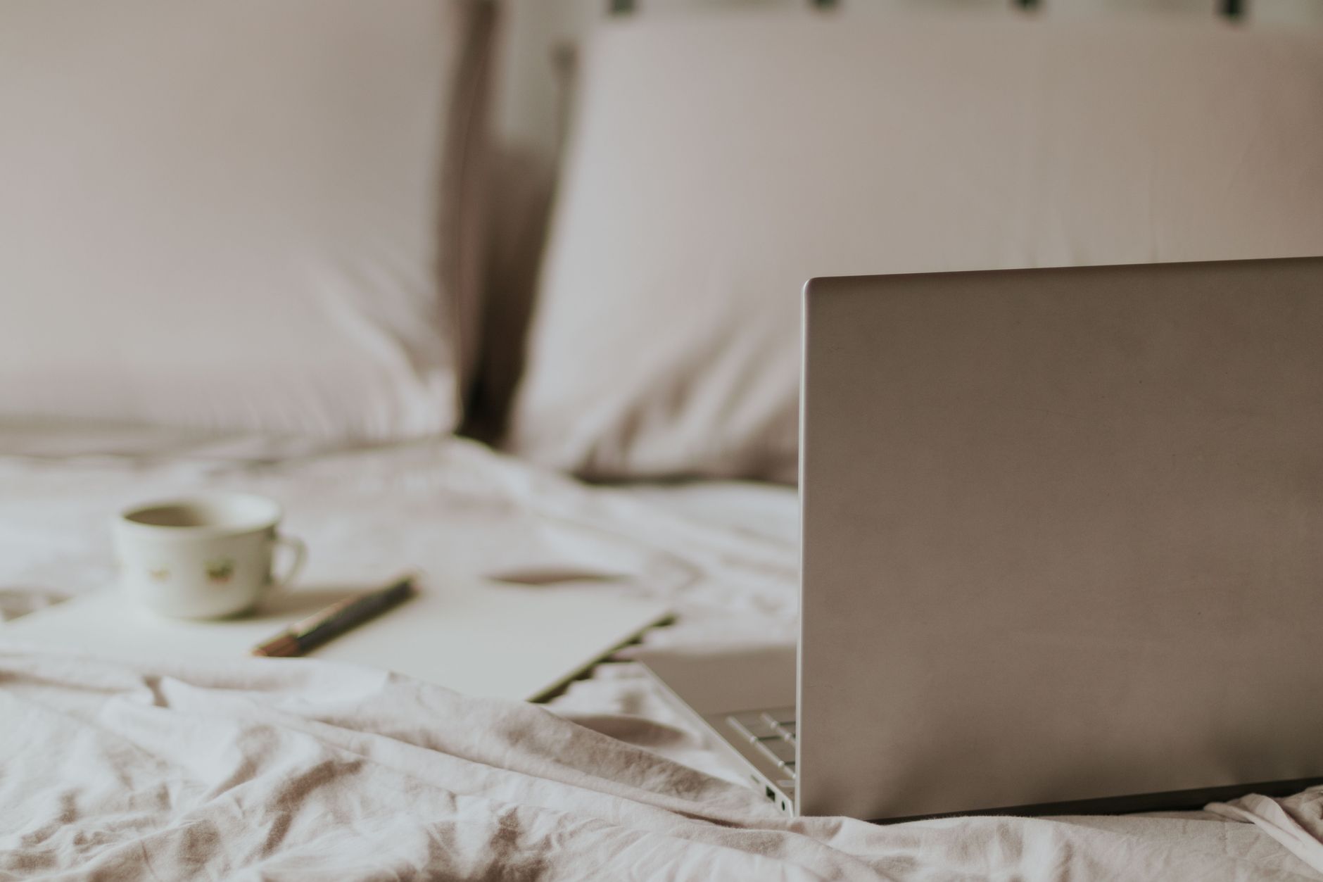 Un salon confortable avec un ordinateur portable, une tasse de café et un carnet sur un lit, ambiance télétravail détendue.