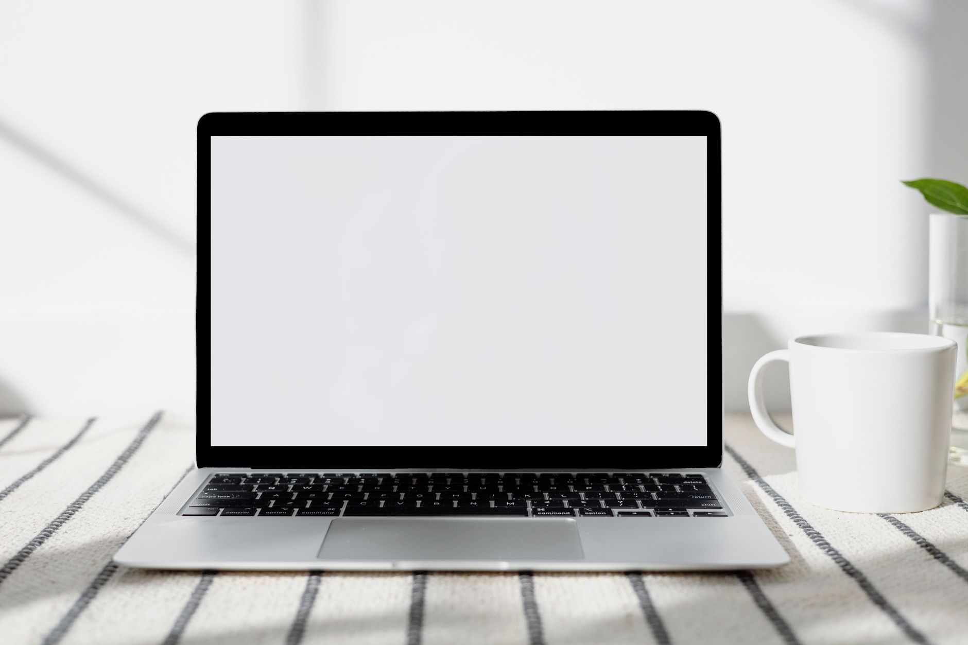 Un bureau minimaliste à domicile avec un ordinateur portable à écran vide et une tasse, baigné de lumière naturelle.